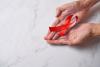 World AIDS Day awareness red ribbon: pair of hands holding red ribbon over a marble top